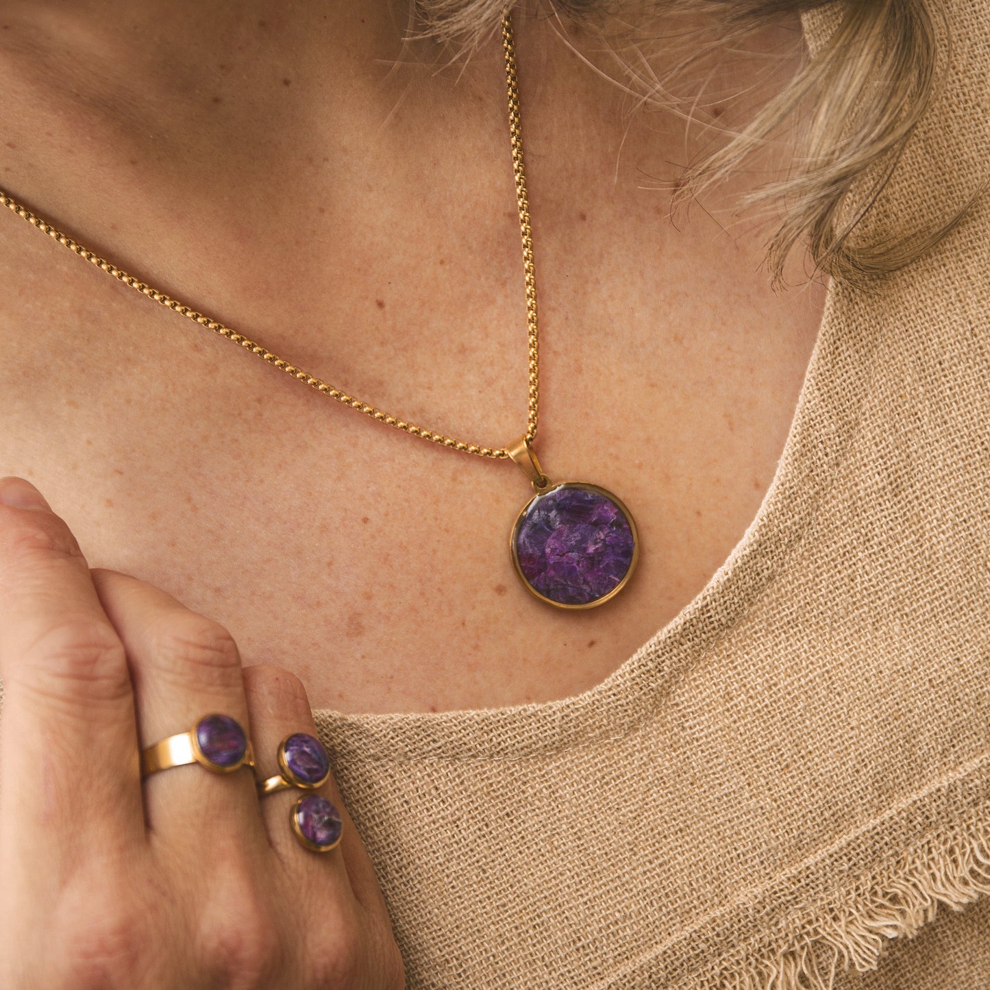 Close-up of a person wearing a gold necklace with a purple pendant and matching ring.