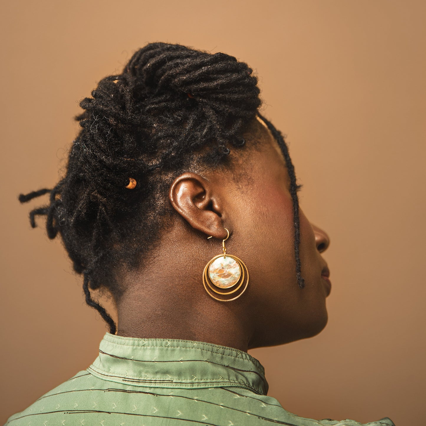 Profile of a person with braided hair wearing gold earrings against a brown background