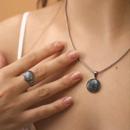 Woman wearing a necklace with a pendant and a ring on her finger, against a neutral background.