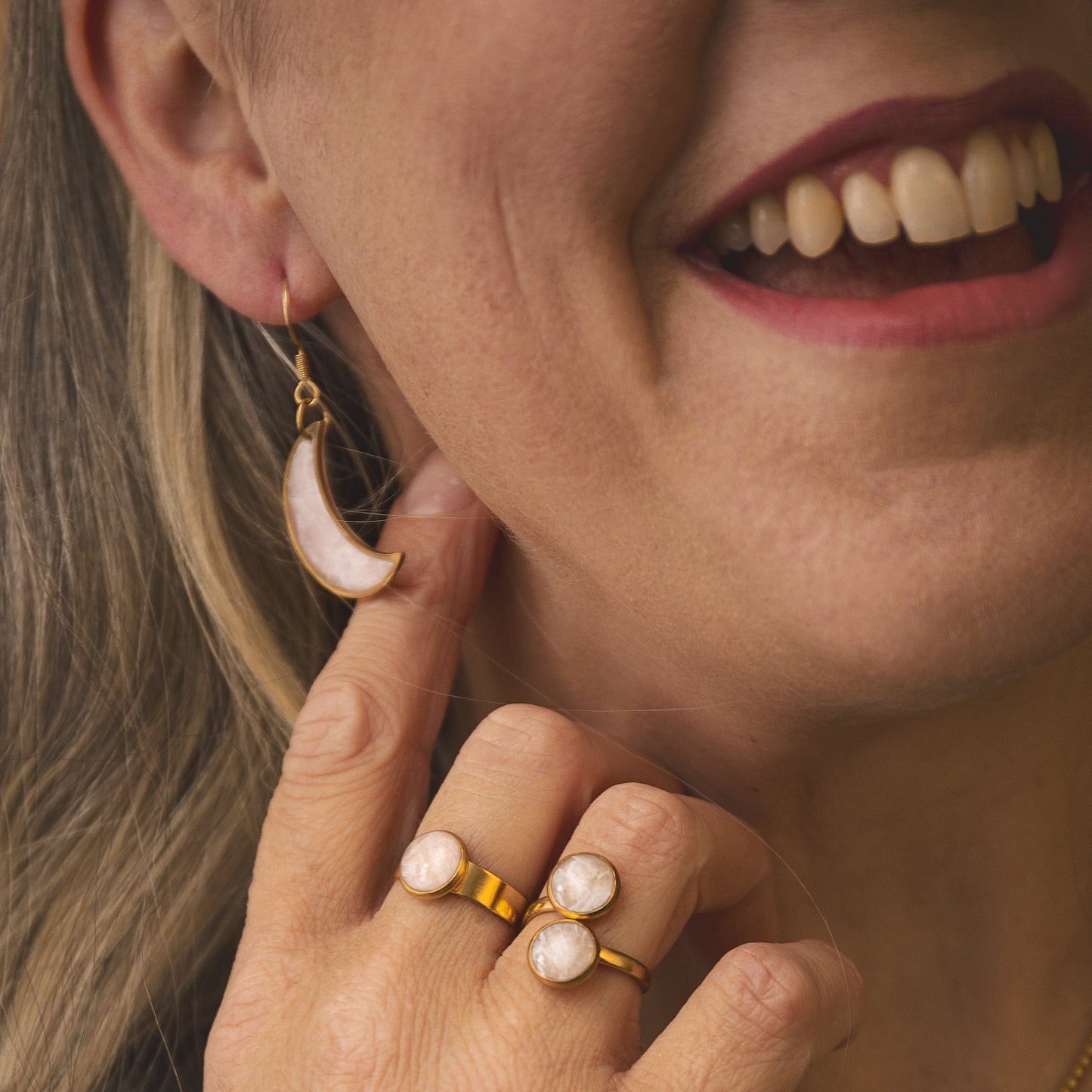 Woman wearing gold jewelry with pearl accents, including earrings, ring, and necklaces.