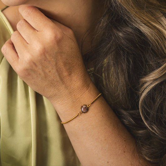 Woman with wavy hair wearing gold earrings and a bracelet against a brown background