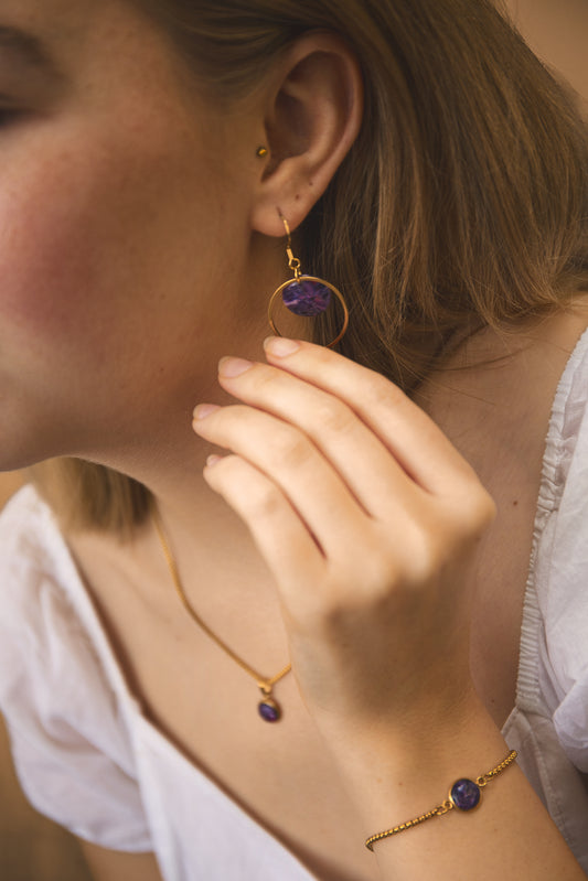 Close-up of a person wearing gold earrings and a matching necklace with purple stones.