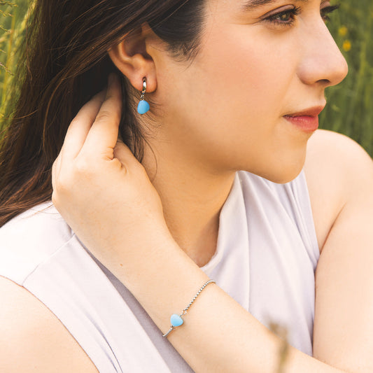 Woman wearing turquoise earrings and a bracelet, sitting outdoors.