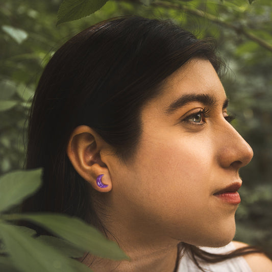 Woman with a purple earring looking to the side with green foliage in the background